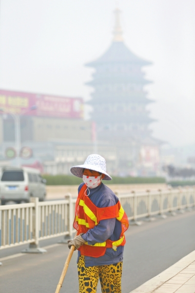 近日，在古都洛陽，環(huán)衛(wèi)工人身后的“天堂”被霧霾籠罩著。