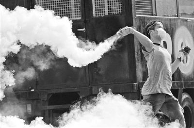 12月2日，泰國(guó)曼谷，一名反政府示威者在總理府附近向負(fù)責(zé)執(zhí)勤的警察投擲催淚彈。英拉請(qǐng)求示威者不要再試圖占領(lǐng)政府工作部門，不要逼迫政府工作人員選邊站。