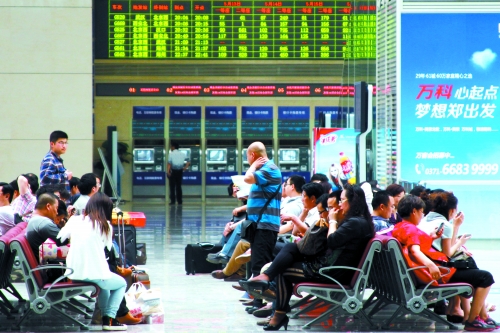 候車(chē)大廳溫度很高，一名乘客一手扇風(fēng)、一手擦汗