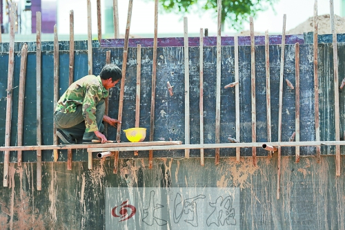　　烈日下，狹窄的架子上，工人正用錘子固定樁基。