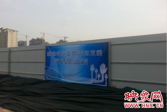 道路南側(cè)圍起了白色的圍擋，墻上標(biāo)示著“因地鐵施工帶來的不便敬請(qǐng)您諒解”的提示牌。