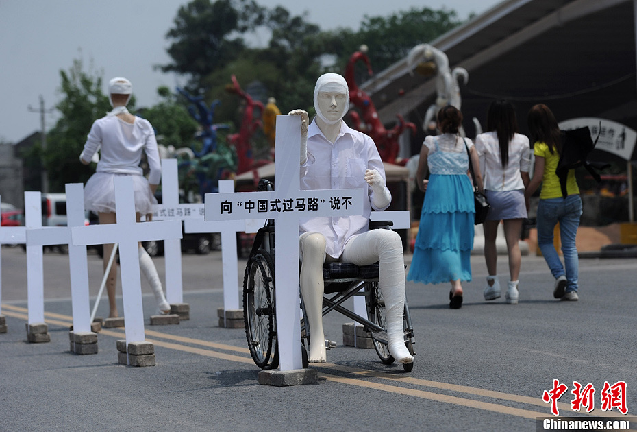 4月16日，重慶市洋人街上擺放著兩個(gè)受了傷的塑料人像“模特”，旁邊十字架上寫(xiě)著向“中國(guó)式過(guò)馬路”說(shuō)不