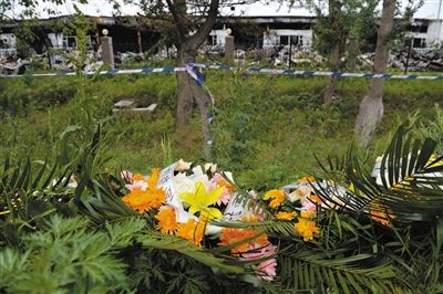 昨日，吉林省德惠市吉林寶源豐禽業(yè)有限公司燃燒事故現(xiàn)場(chǎng)警戒線外，遇難者家屬在路邊擺放了花圈祭奠逝去的親人。吳江 攝