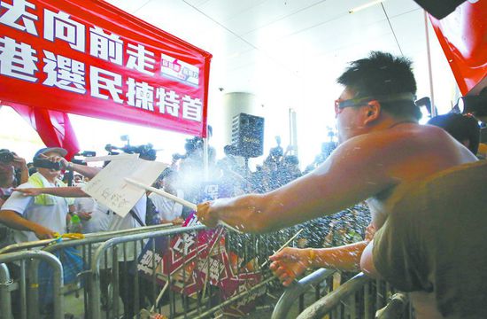 17日，在香港立法會外，一名反對政改的男子向支持派人群投擲標牌。
