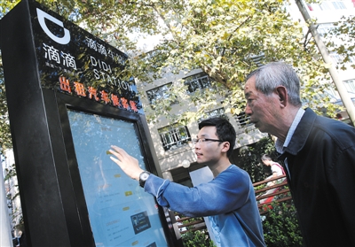 10月15日，滴滴工作人員（左）指導(dǎo)乘客使用“滴滴車站”的電子屏預(yù)約出租車。