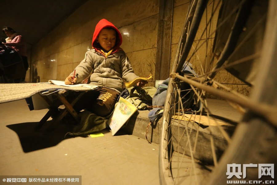 2015年11月8日晚，鄭州，7歲男孩涵洞橋下陪父母練攤，路邊燈下坐小馬扎上寫作業(yè)。