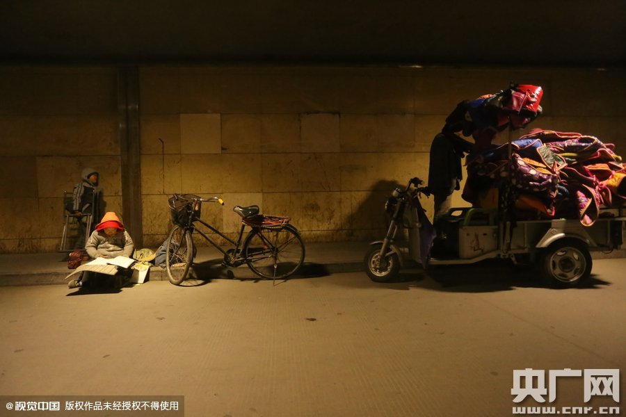 2015年11月8日晚，鄭州，7歲男孩涵洞橋下陪父母練攤，路邊燈下坐小馬扎上寫作業(yè)。