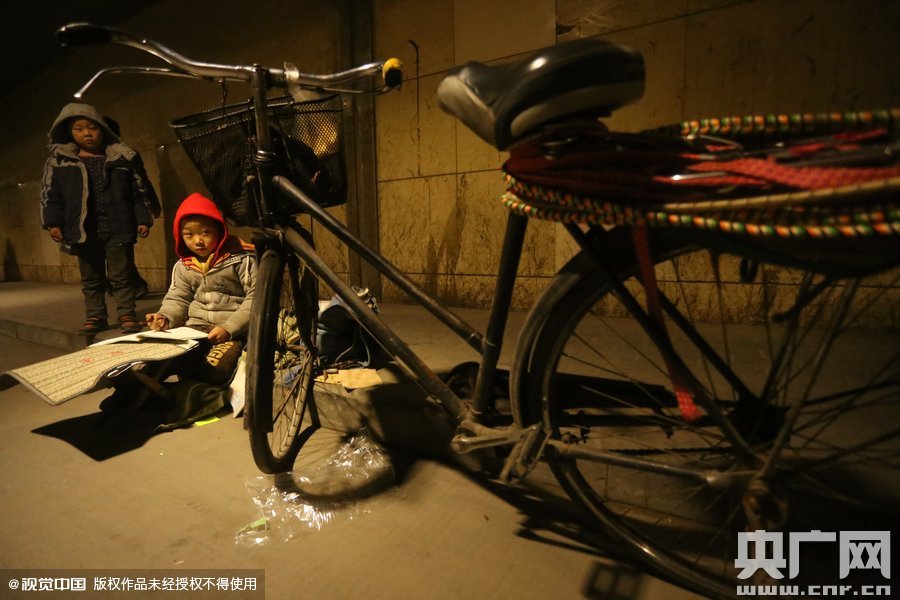 2015年11月8日晚，鄭州，7歲男孩涵洞橋下陪父母練攤，路邊燈下坐小馬扎上寫作業(yè)。