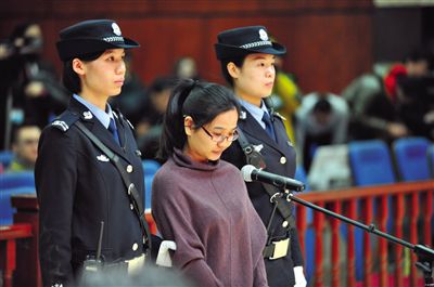 被告人盧梅低著頭，站在朝陽法院刑事審判庭的被告席上。