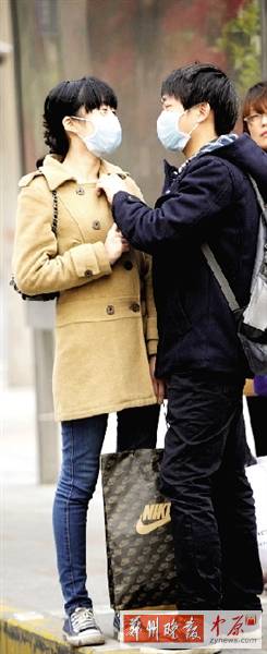 公交站臺(tái)上，一對(duì)年輕人戴著口罩，系緊衣領(lǐng)。